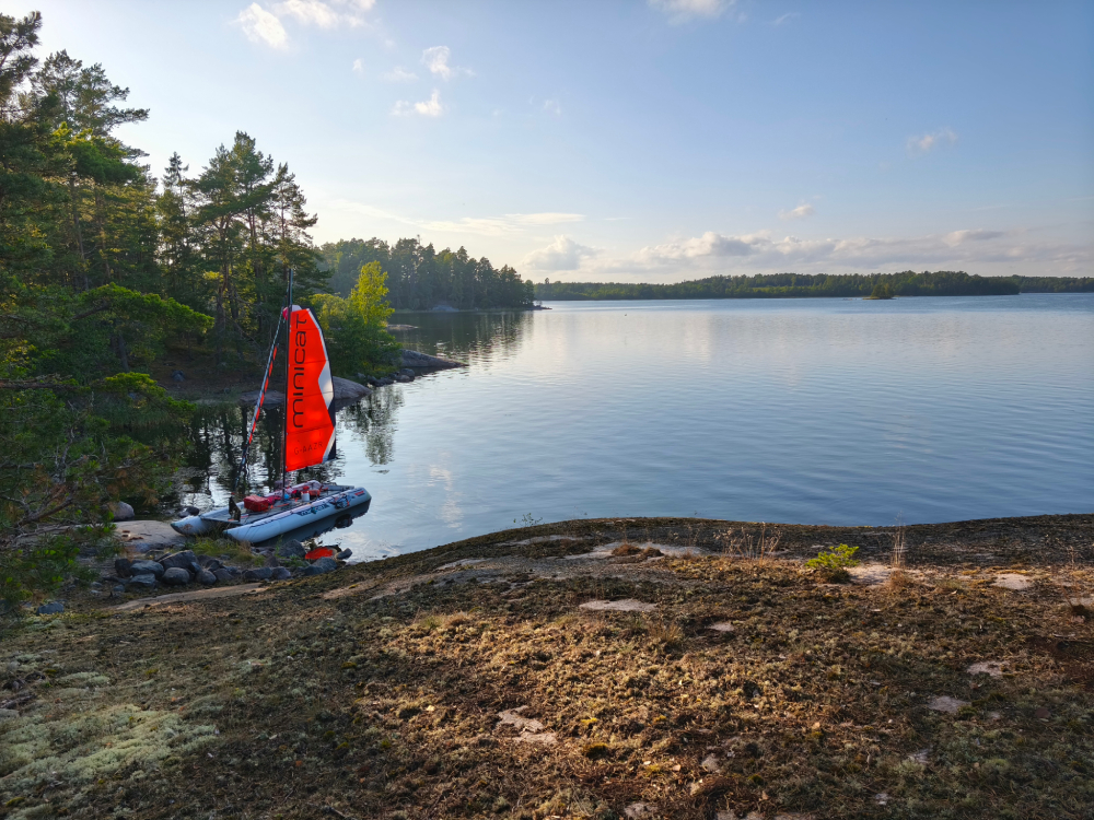 MiniCat anchored at sunset among granite rocks and pine trees in the Baltic Sea.